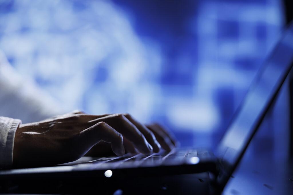 A computer operator is using a laptop in a setting that emphasizes technology and cybersecurity. The scene includes a close-up of hands typing on the keyboard.