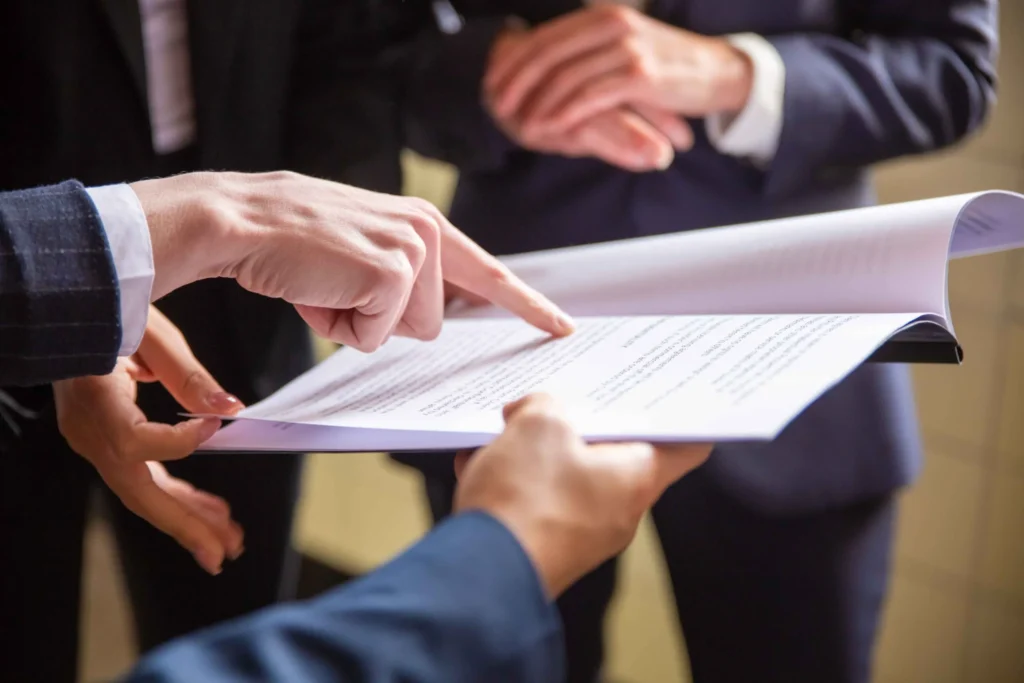 Close up of business people in suits reviewing a printed document, one hand pointing at the text
