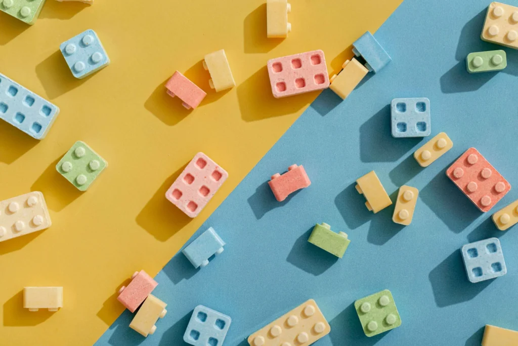 Flat lay of pastel toy building block shaped pieces scattered across a split yellow and blue background