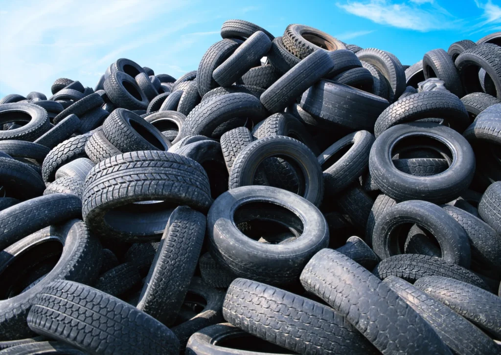 Large pile of worn used car tires heaped outdoors under a blue sky with light clouds